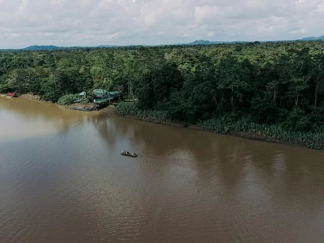 Veduta aerea di una barca su un fiume marrone circondato da foresta fitta.